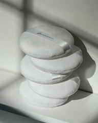 Vier gestapelte weiße Puderquasten, oberste Quaste mit Glo Skin Beauty Logo.