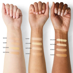 Drei Unterarme mit sechs Foundation-Swatches, beschriftet mit Beige, Sand, Golden, Natural, Honey und Tawny