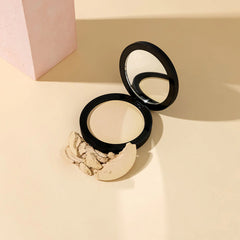 Geöffneter Kompaktpuder mit Spiegel und zerstoßenem hellbeigen Puder auf beigefarbener Oberfläche