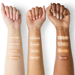 Drei Unterarme mit Foundation-Swatches, beschriftet mit Alabaster, Porcelain, Linen, Naturelle, Almond, Tahini, Brûlée, Café, Caramel und Mocha