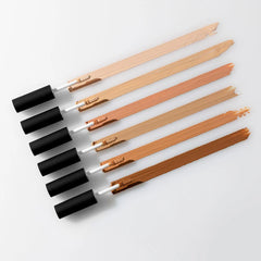 Sechs Concealer-Applikator-Swatches in einem Bronzeverlauf, diagonal auf weißem Hintergrund angeordnet