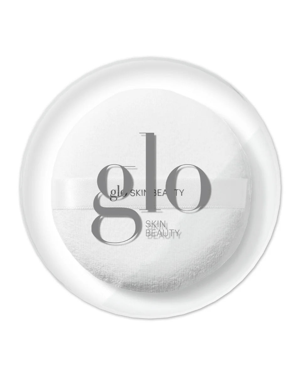 Weiße Puderquaste mit Schleifenband und Glo Skin Beauty Logo, präsentiert in einer transparenten runden Dose.