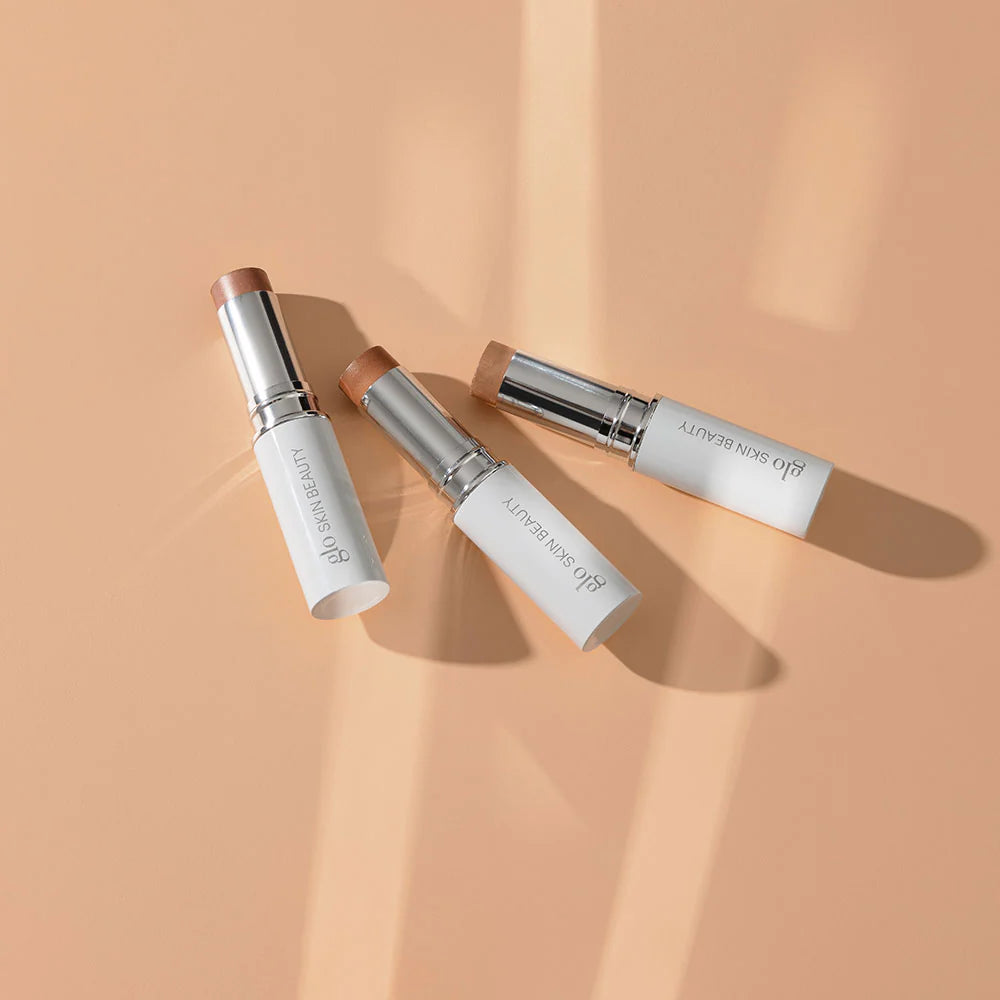 Glo Skin Beauty Skin Glow Stick Highlighter: Drei Creme-Highlighter-Stifte auf Pfirsich-Hintergrund