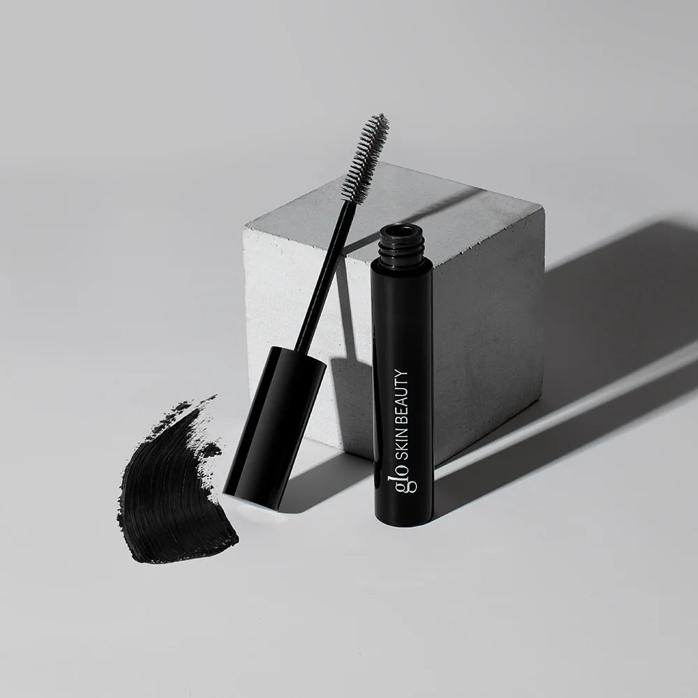 Glo Skin Beauty Mascara in schwarzer Tube mit separatem Bürstchen und schwarzem Farbswatch, Aufdruck Glo Skin Beauty auf der Verpackung.